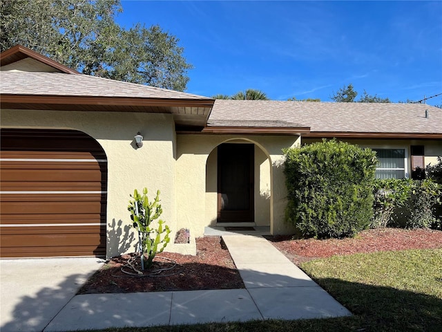 entrance to property featuring a garage, a shingled roof, and stucco siding