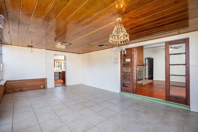 tiled spare room with wood walls, wood ceiling, a wood stove, and an inviting chandelier