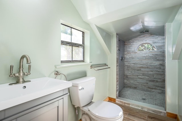 bathroom with a tile shower, wood-type flooring, vaulted ceiling, toilet, and vanity