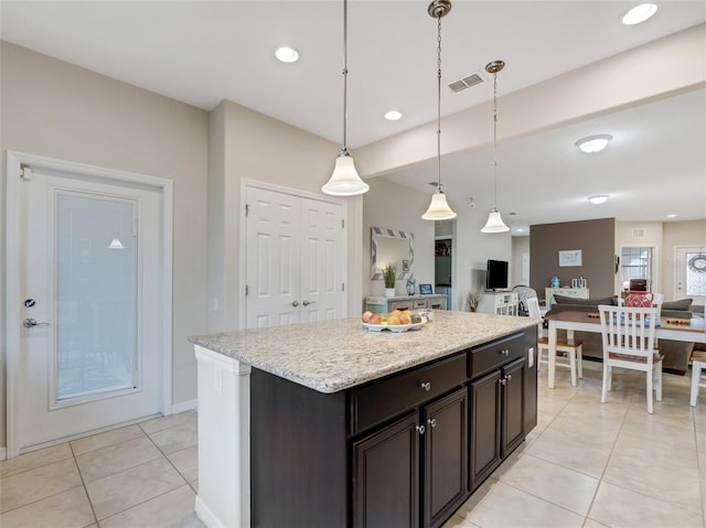 kitchen with light stone counters, dark brown cabinets, light tile patterned floors, decorative light fixtures, and a kitchen island