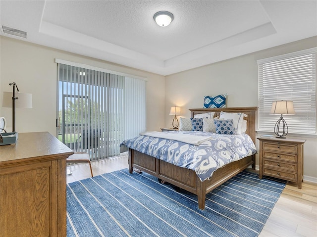 bedroom with a tray ceiling, access to outside, a textured ceiling, and light wood-type flooring