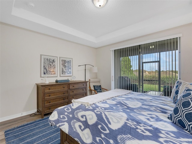 bedroom featuring access to exterior, wood-type flooring, and a raised ceiling