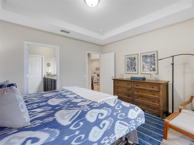 bedroom with a tray ceiling, ensuite bathroom, and a textured ceiling