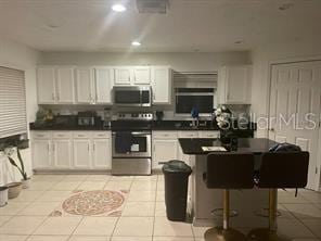 kitchen featuring appliances with stainless steel finishes, light tile patterned floors, white cabinetry, and a breakfast bar area