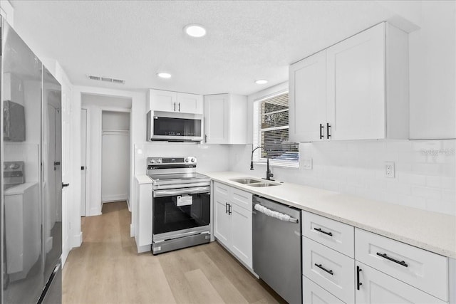 kitchen with white cabinetry, sink, washer / clothes dryer, appliances with stainless steel finishes, and light wood-type flooring