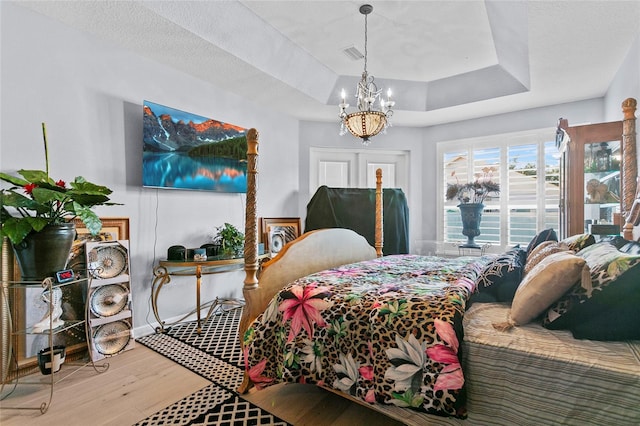 bedroom featuring a textured ceiling, hardwood / wood-style flooring, an inviting chandelier, and a tray ceiling