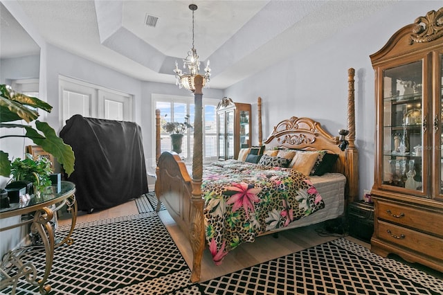 bedroom with a raised ceiling, light wood-type flooring, a textured ceiling, and an inviting chandelier