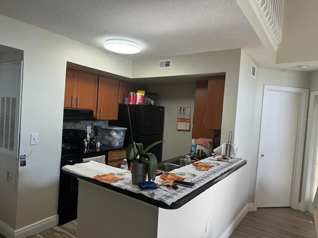 kitchen with backsplash, black refrigerator, a textured ceiling, light hardwood / wood-style floors, and kitchen peninsula