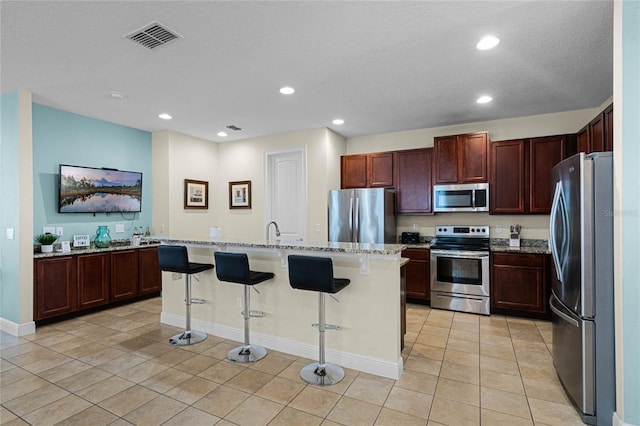 kitchen featuring light stone countertops, appliances with stainless steel finishes, a kitchen island with sink, and a breakfast bar area