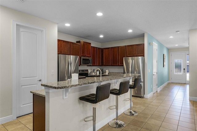 kitchen with a kitchen breakfast bar, light tile patterned floors, stainless steel appliances, and a kitchen island with sink