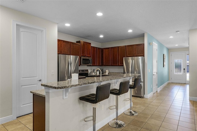 7639 Wilmington Loop, Kissimmee, FL 34747 - kitchen featuring appliances with stainless steel finishes, light tile patterned floors, a kitchen bar, dark stone countertops, and recessed lighting