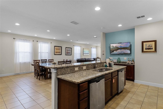 kitchen with dishwasher, sink, light stone countertops, light tile patterned floors, and an island with sink