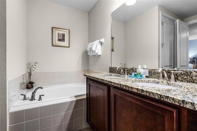 bathroom with tiled tub, vanity, and a textured ceiling