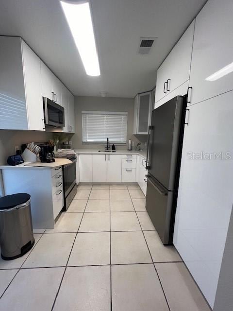 kitchen featuring light tile patterned floors, stainless steel appliances, white cabinetry, and sink