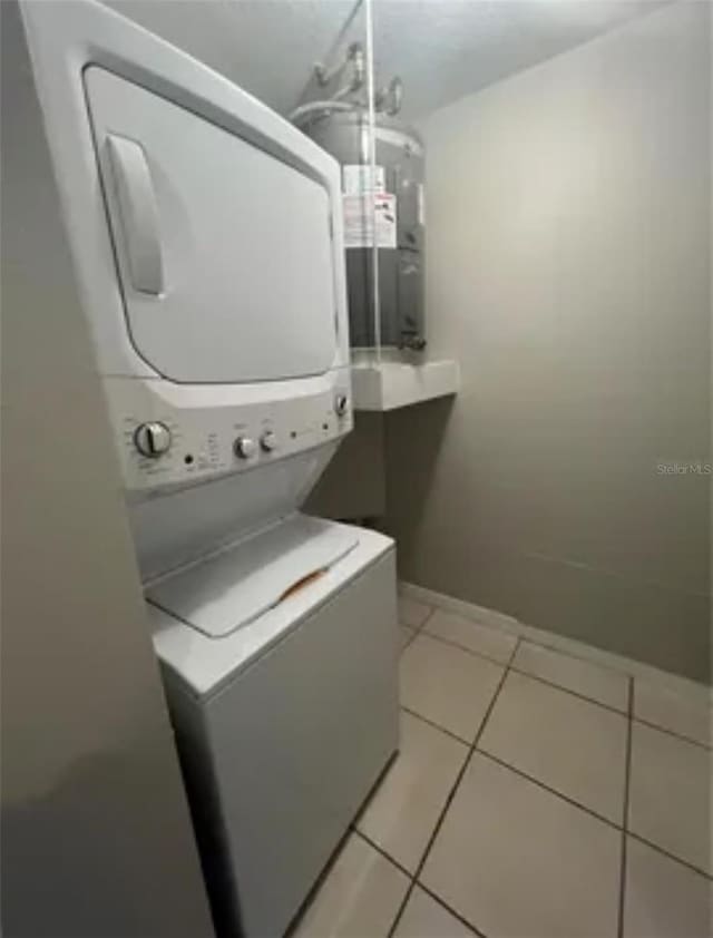 clothes washing area with electric water heater, stacked washing maching and dryer, and light tile patterned floors