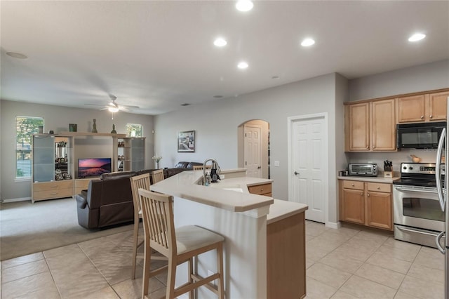 kitchen featuring a kitchen breakfast bar, ceiling fan, sink, electric stove, and a center island with sink