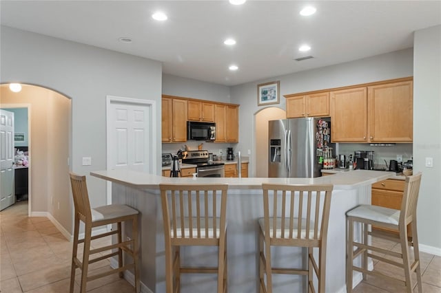 kitchen with a kitchen bar, appliances with stainless steel finishes, a center island, and light tile patterned floors