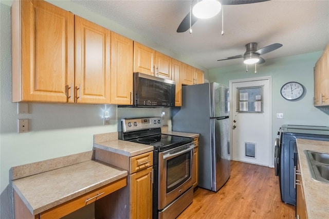 kitchen with ceiling fan, sink, stainless steel appliances, washing machine and dryer, and light hardwood / wood-style floors