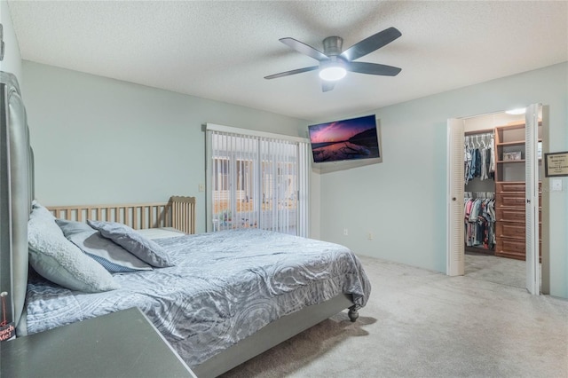 carpeted bedroom with a textured ceiling, a walk in closet, a closet, and ceiling fan