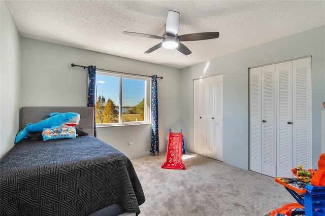 carpeted bedroom with a textured ceiling, ceiling fan, and two closets