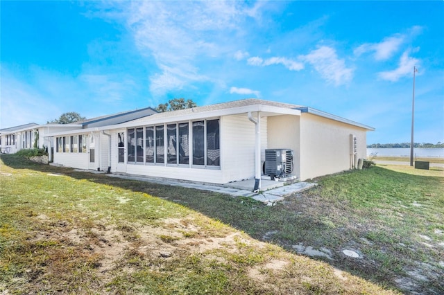 back of house featuring a sunroom, a water view, central AC, and a lawn