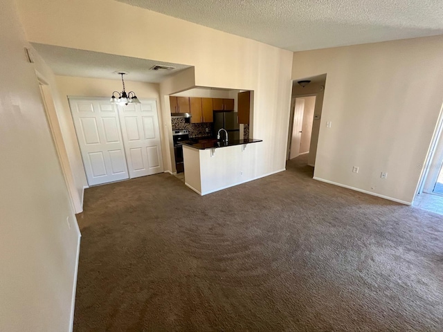 unfurnished living room featuring an inviting chandelier, a textured ceiling, and dark colored carpet