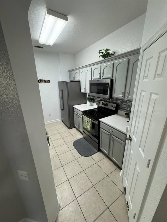 kitchen featuring backsplash, gray cabinetry, light tile patterned flooring, and appliances with stainless steel finishes