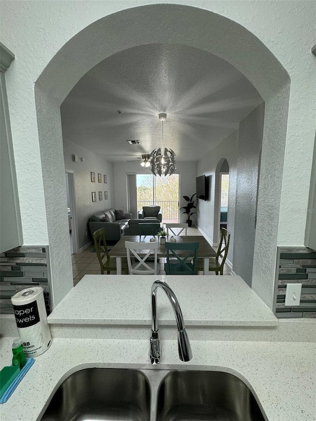 kitchen with light stone countertops, sink, tile patterned flooring, backsplash, and a textured ceiling