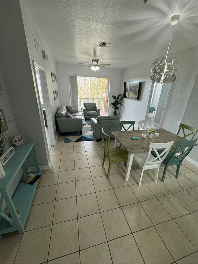 dining space with ceiling fan with notable chandelier, light tile patterned floors, and a textured ceiling