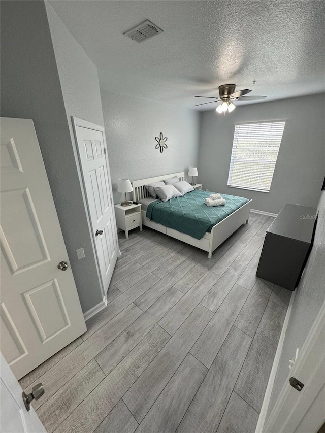 bedroom with ceiling fan, light hardwood / wood-style floors, and a textured ceiling