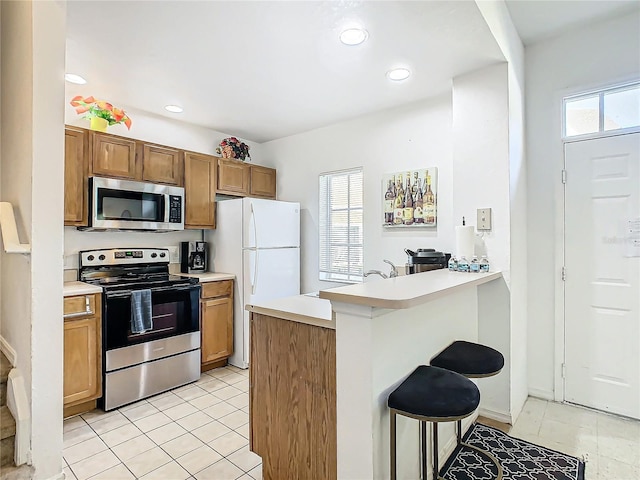 kitchen with a kitchen breakfast bar, kitchen peninsula, light tile patterned floors, and stainless steel appliances