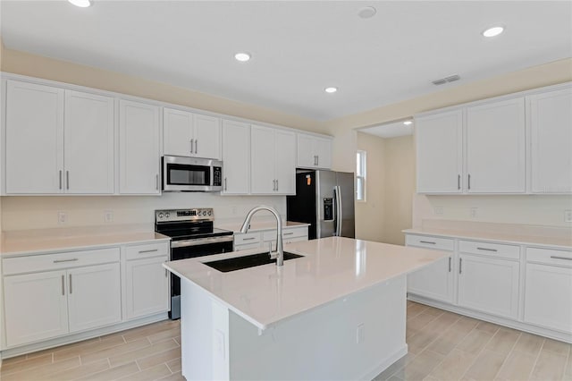 kitchen with stainless steel appliances, white cabinetry, and a center island with sink