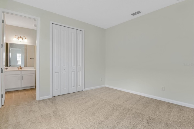 unfurnished bedroom with a closet, light carpet, and ensuite bath