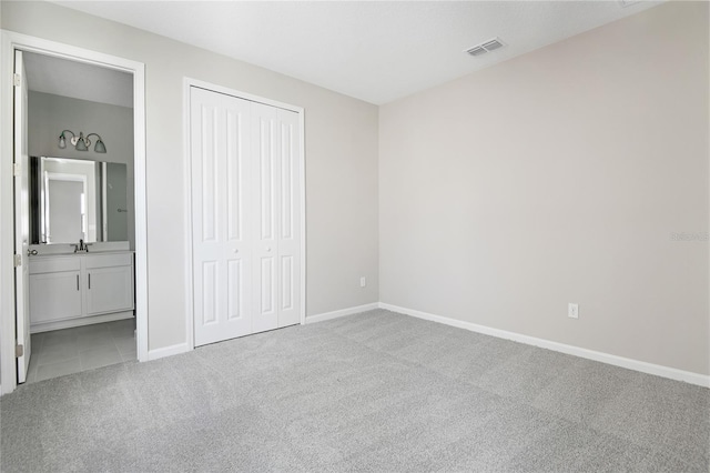 unfurnished bedroom featuring connected bathroom, a closet, light colored carpet, and sink