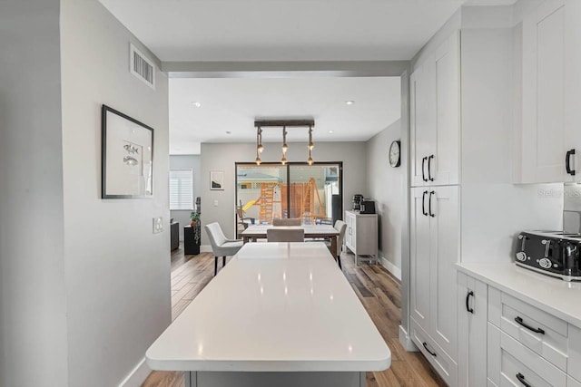 kitchen with decorative light fixtures, light hardwood / wood-style floors, a kitchen island, and white cabinetry