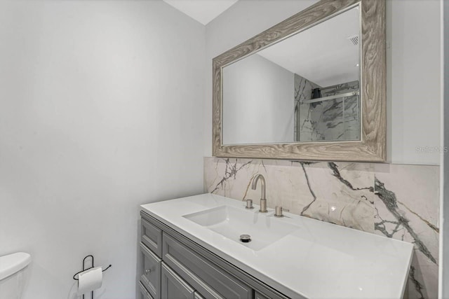 bathroom featuring vanity, toilet, a shower with shower door, and backsplash