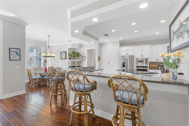 kitchen with kitchen peninsula, appliances with stainless steel finishes, dark hardwood / wood-style flooring, dark stone counters, and white cabinetry