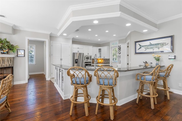 kitchen with appliances with stainless steel finishes, white cabinetry, ornamental molding, and dark wood-type flooring