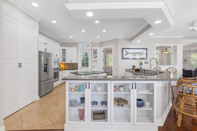 kitchen featuring white cabinetry, stainless steel appliances, dark stone counters, a breakfast bar area, and light tile patterned flooring