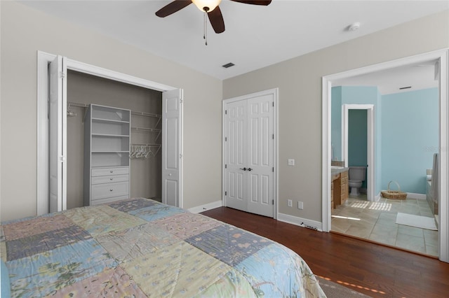 bedroom featuring connected bathroom, ceiling fan, dark hardwood / wood-style flooring, and two closets