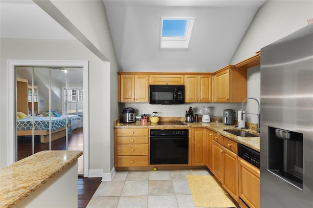 kitchen with light stone counters, lofted ceiling with skylight, sink, black appliances, and light hardwood / wood-style flooring