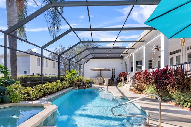 view of pool featuring glass enclosure, ceiling fan, and an outdoor kitchen