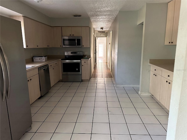 kitchen with a textured ceiling, light tile patterned floors, and stainless steel appliances