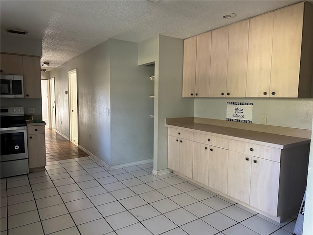 kitchen with light brown cabinetry, light tile patterned flooring, a textured ceiling, and appliances with stainless steel finishes