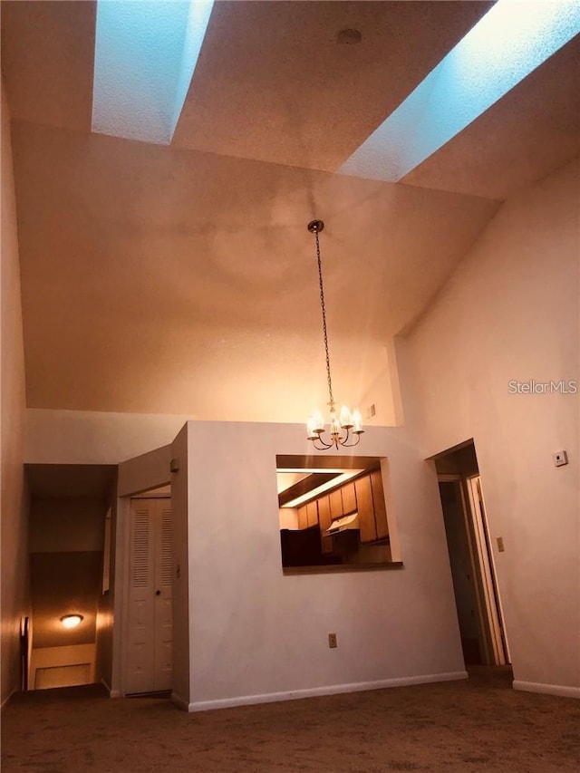 unfurnished living room featuring a chandelier, high vaulted ceiling, a skylight, and dark carpet