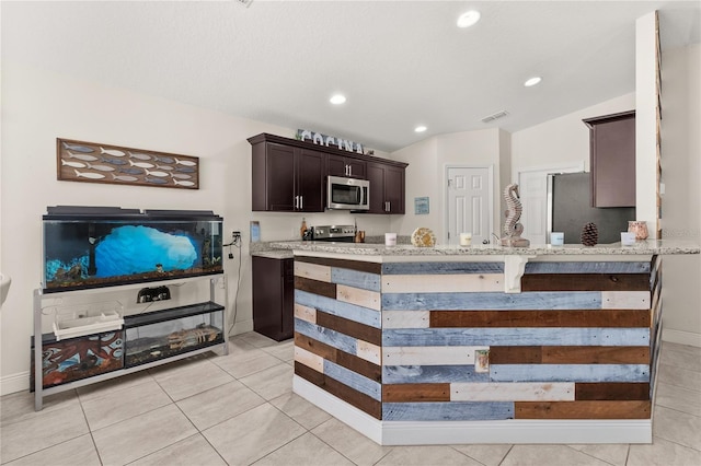 kitchen with stainless steel appliances, light stone counters, lofted ceiling, dark brown cabinets, and light tile patterned floors