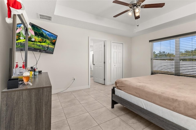 bedroom featuring ceiling fan, a raised ceiling, light tile patterned floors, and ensuite bath