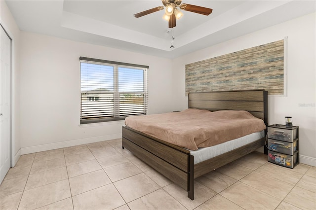 bedroom with ceiling fan, light tile patterned floors, and a tray ceiling