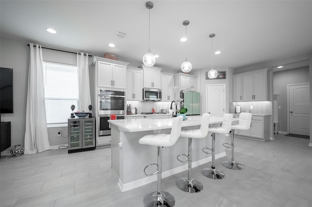 kitchen with pendant lighting, white cabinetry, stainless steel appliances, and a kitchen island with sink