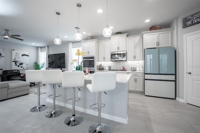 kitchen with white cabinets, appliances with stainless steel finishes, pendant lighting, and an island with sink